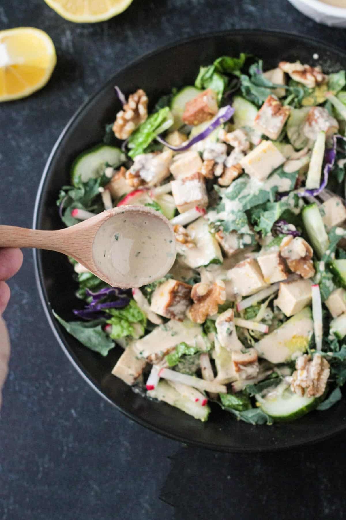 Wooden spoon drizzling salad dressing over a salad.