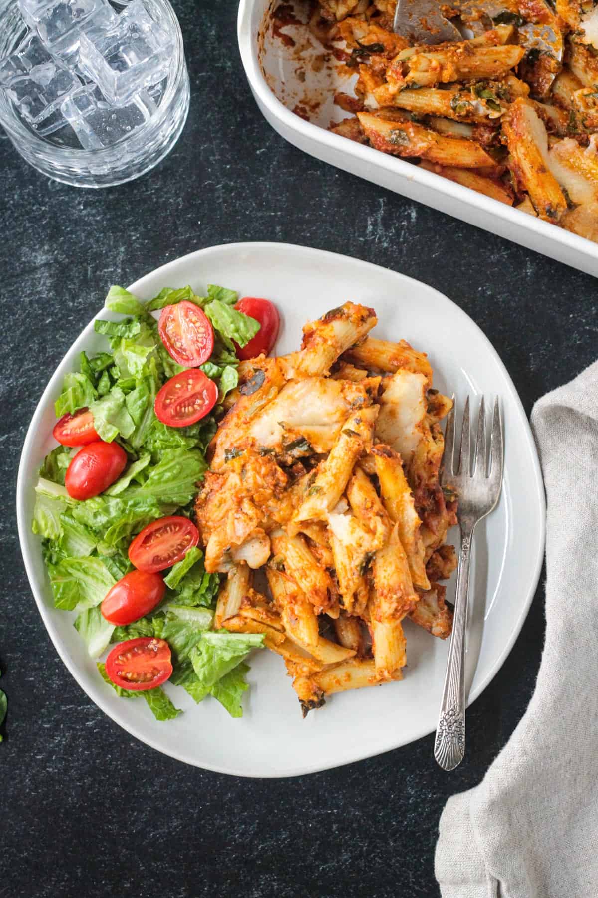 Serving of vegan pasta bake on a plate with salad greens.