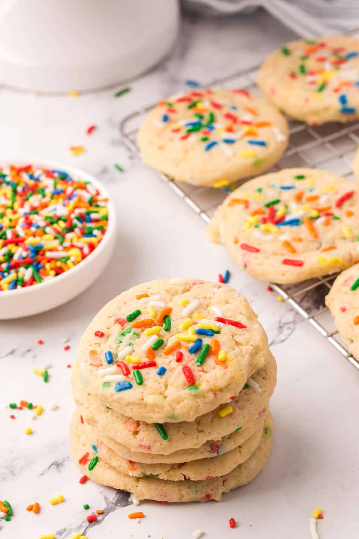 Stack of vegan funfetti sugar cookies in front of a cooling rack of more.