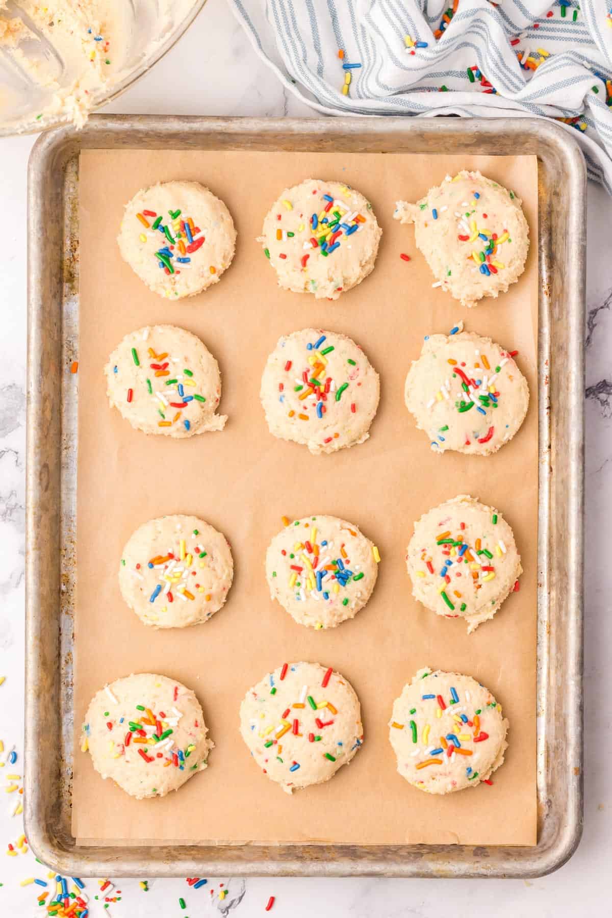 Raw vegan funfetti sugar cookie dough on a parchment lined baking sheet.