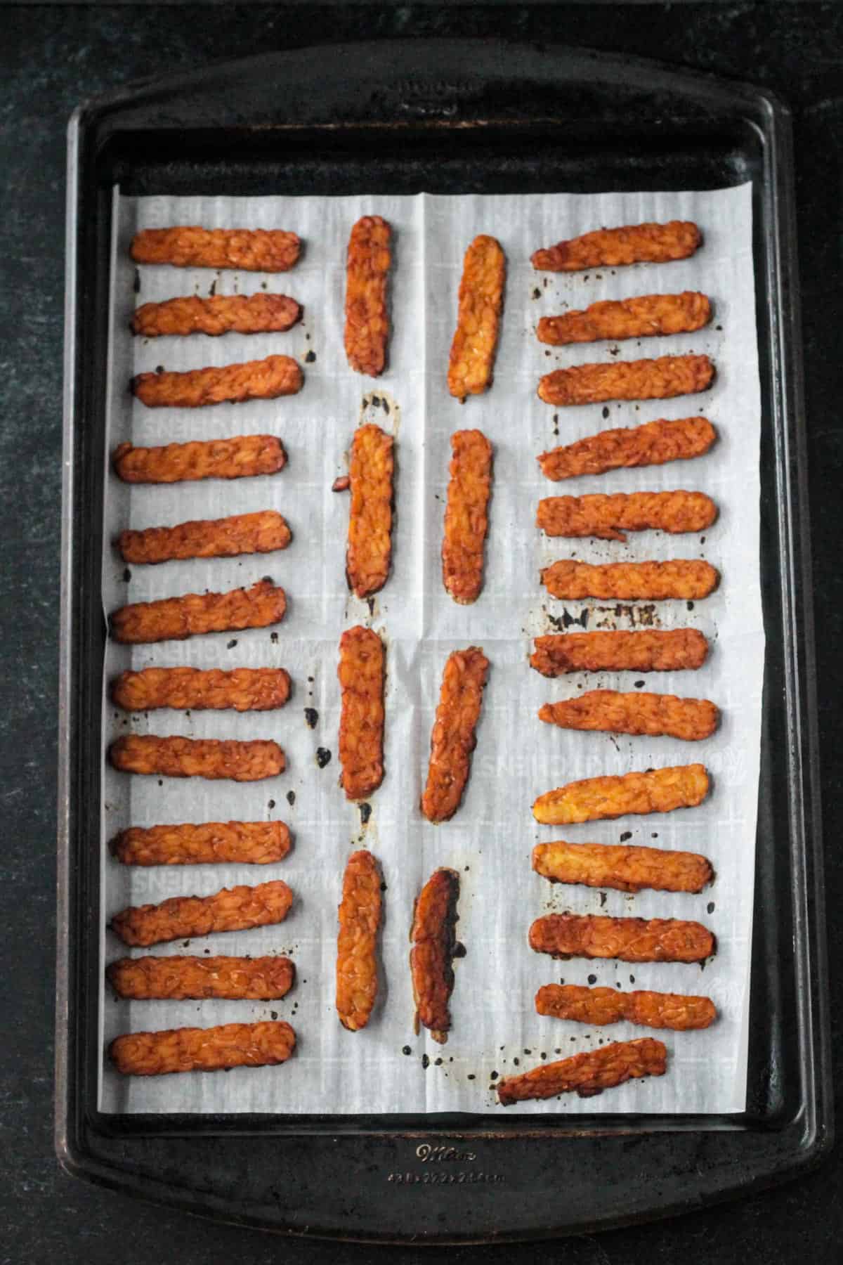 Flipping all the vegan bacon slices on a baking sheet after baking on one side.