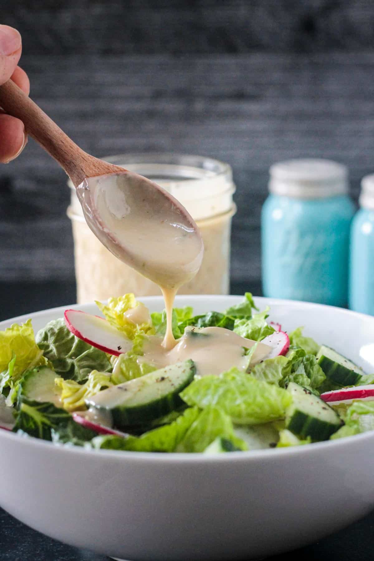 Hummus dressing being drizzled over a salad from a wooden spoon.