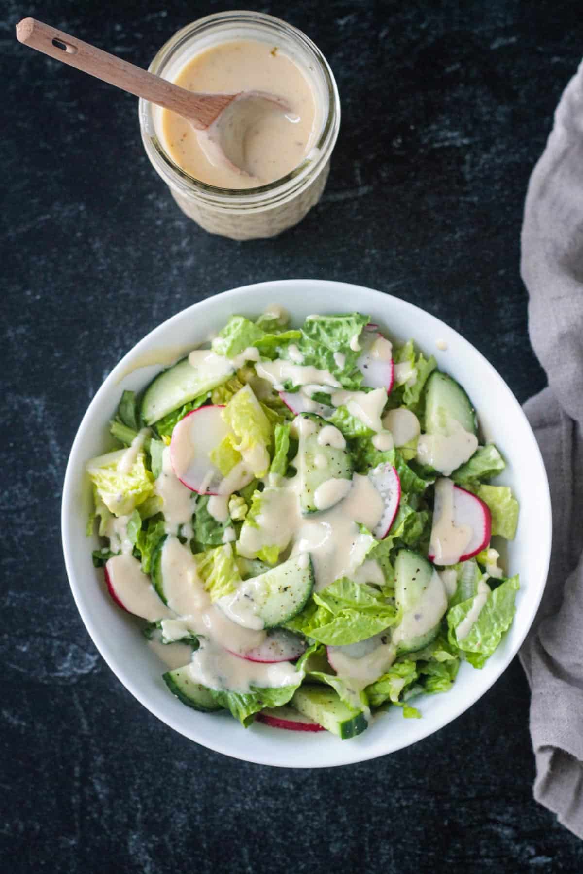 Hummus dressing in a jar next to a bowl of salad.