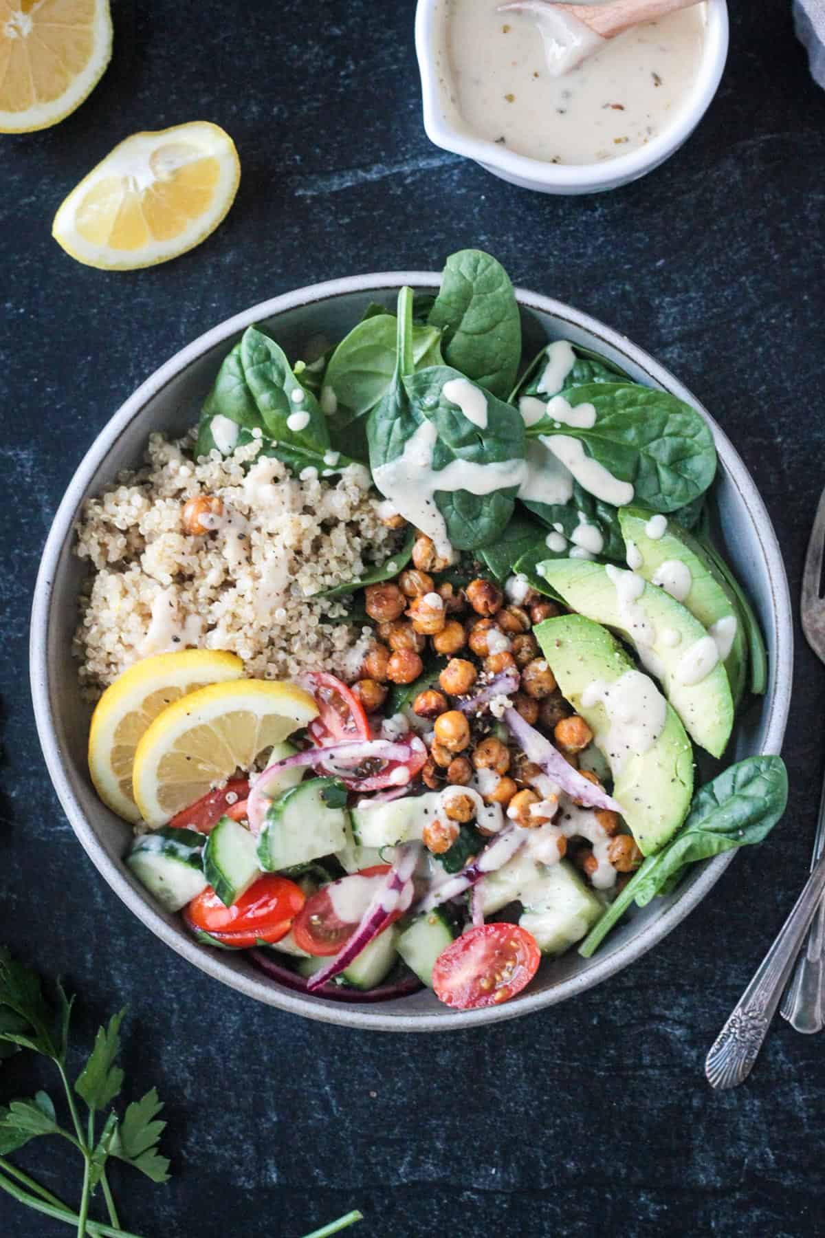 Mediterranean grain bowl with quinoa, chickpeas, cucumber tomato salad, avocado, spinach, and dressing.