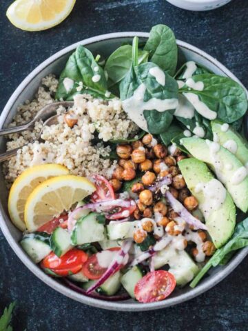 Two forks in a vegan bowl full of grains, veggies, beans, and sauce.