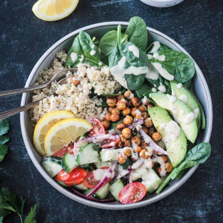 Two forks in a vegan bowl full of grains, veggies, beans, and sauce.