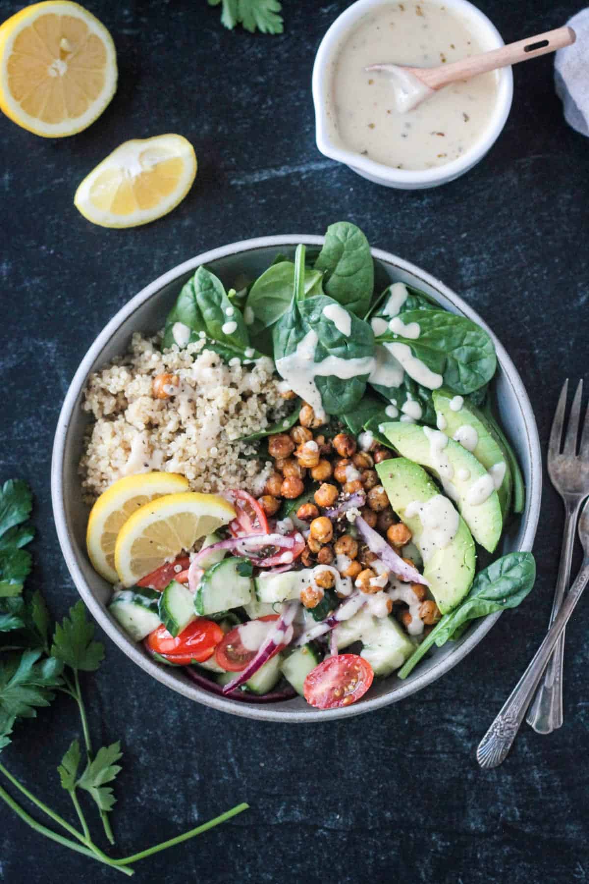 Mediterranean grain bowl with quinoa, chickpeas, cucumber tomato salad, avocado, spinach, and dressing.