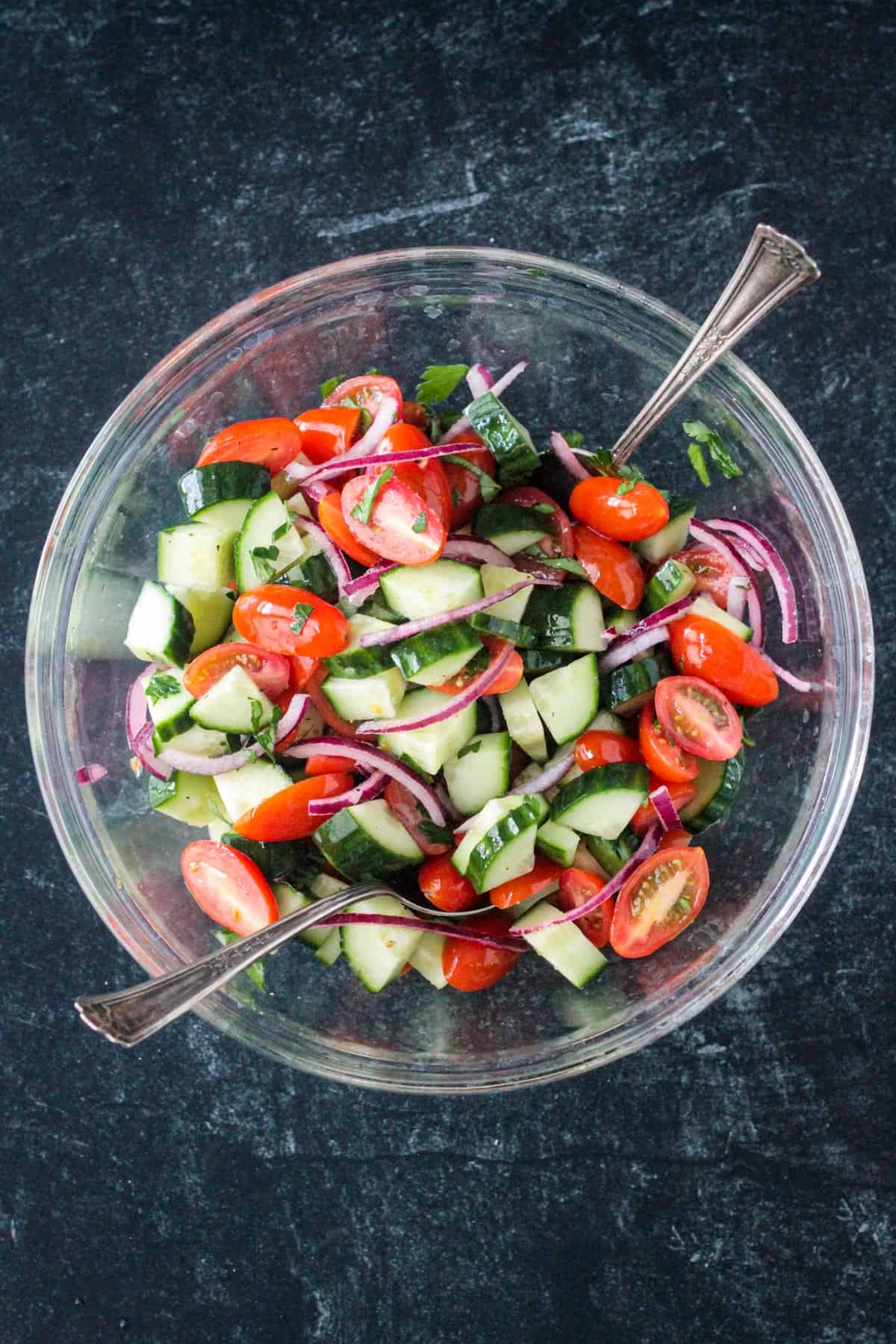 Cucumber tomato salad mixed in a glass bowl.