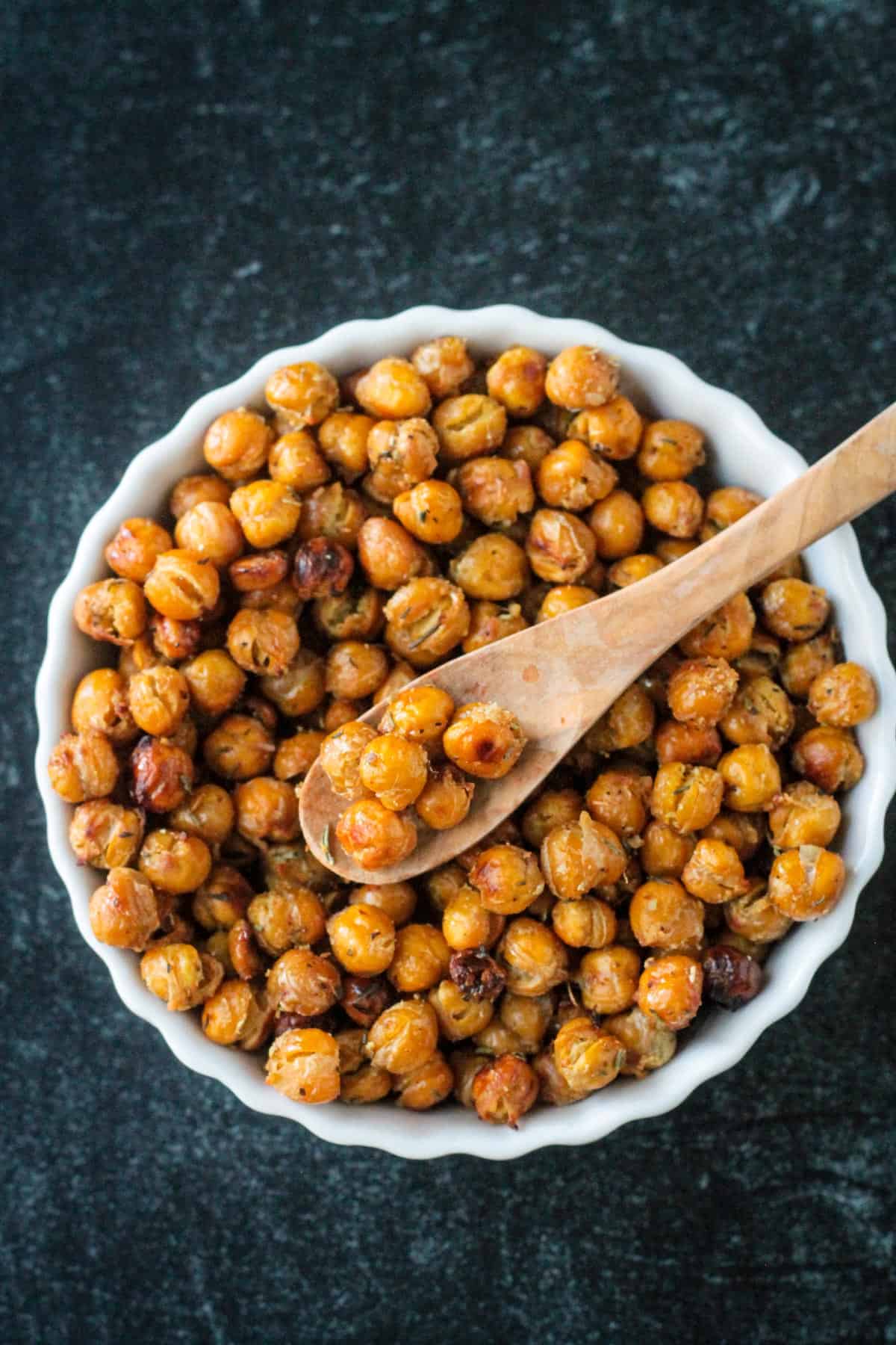 Seasoned roasted chickpeas in a bowl with a small wooden spoon.