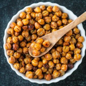 Seasoned roasted chickpeas in a bowl with a small wooden spoon.