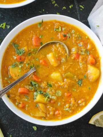 Metal spoon in a bowl of red lentil potato soup.