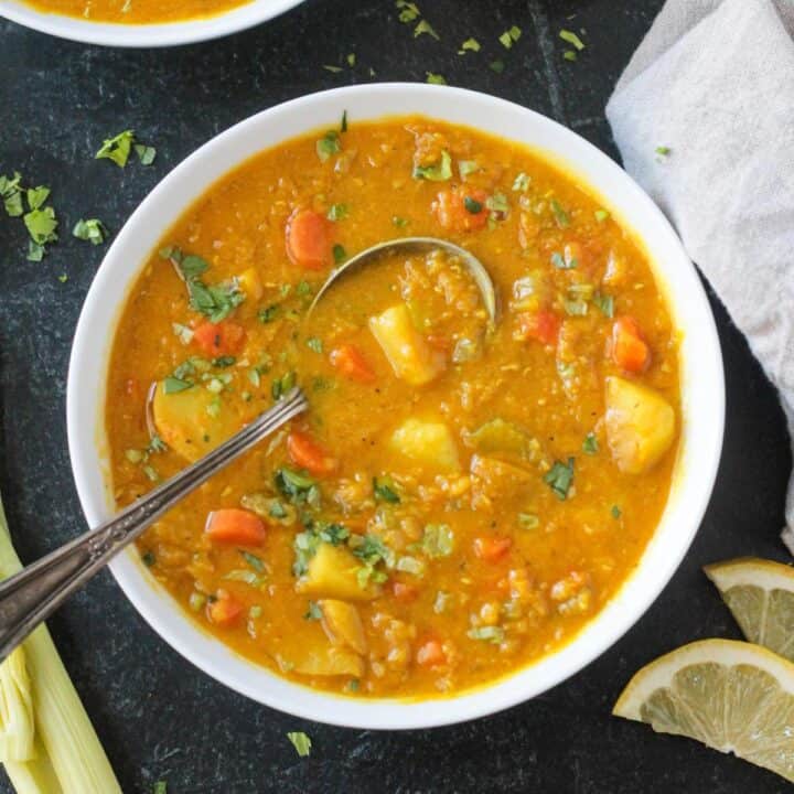 Metal spoon in a bowl of red lentil potato soup.
