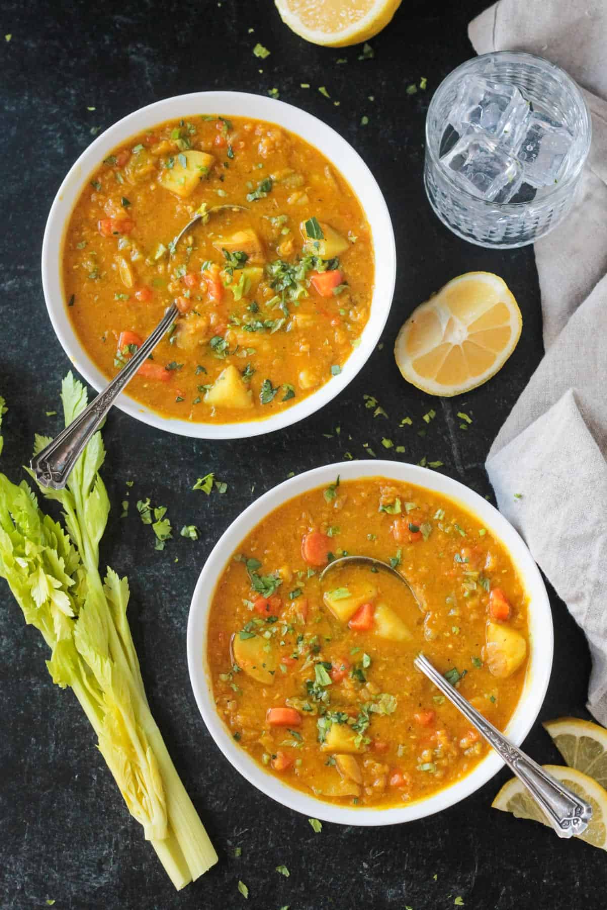 Two bowls of lentil potato soup next to ribs of celery and sliced lemon.