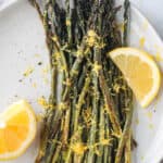 Roasted asparagus with lemon zest and two lemon wedges on a plate.