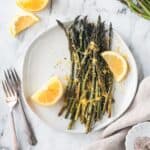 Roasted asparagus with lemon zest and two lemon wedges on a plate.