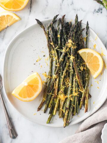 Roasted asparagus with lemon zest and two lemon wedges on a plate.
