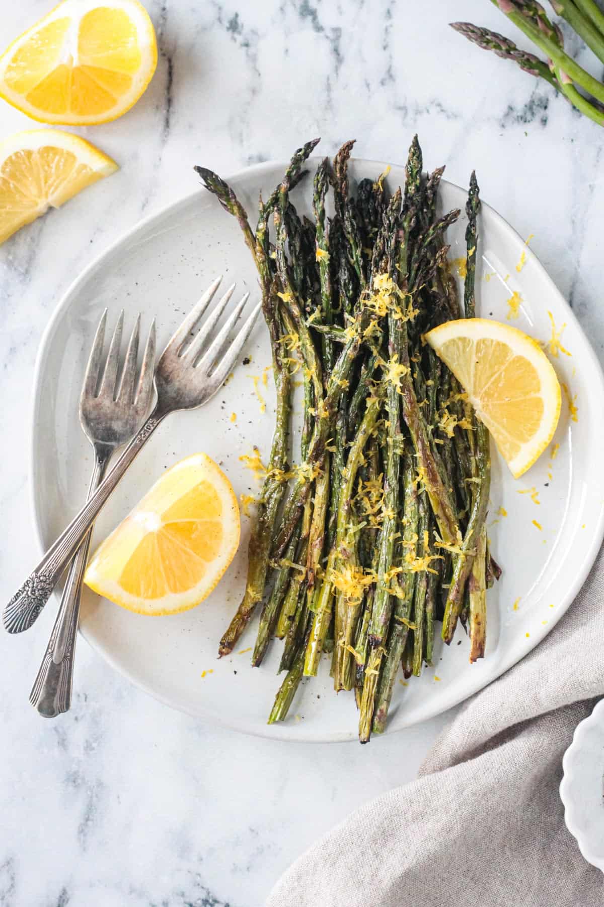Two forks on a plate with roasted asparagus with lemon wedges.