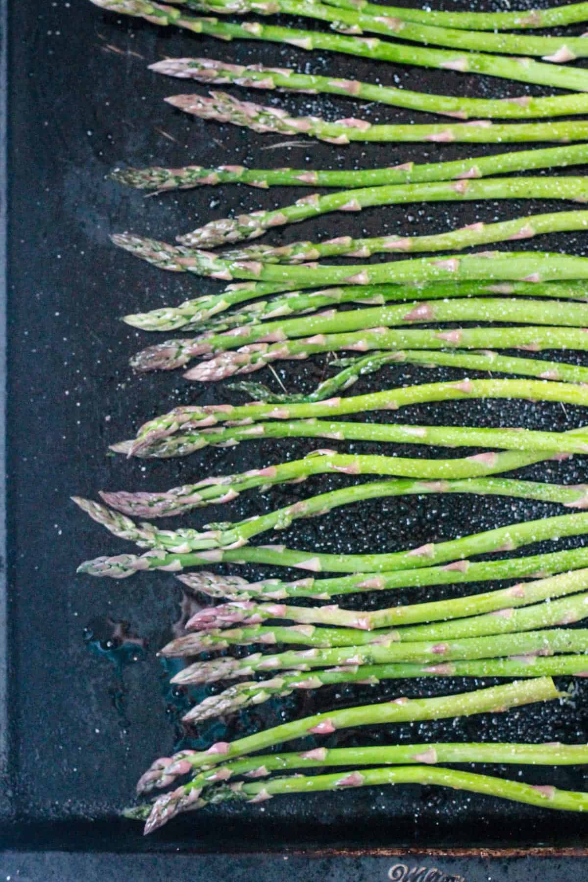 Raw spears with sprinkled with salt and pepper on a baking sheet.