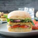 Pesto tofu sandwich on a roll with tomato slices and arugula.