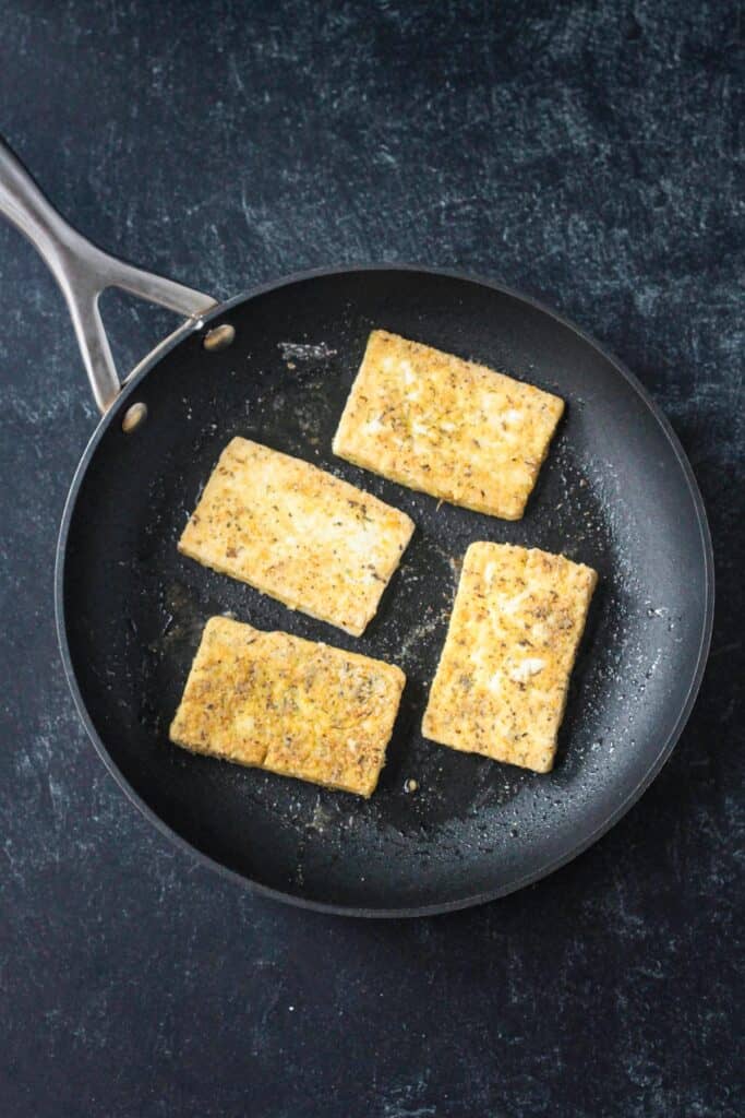 Four slices of tofu in a skillet fried until golden brown.