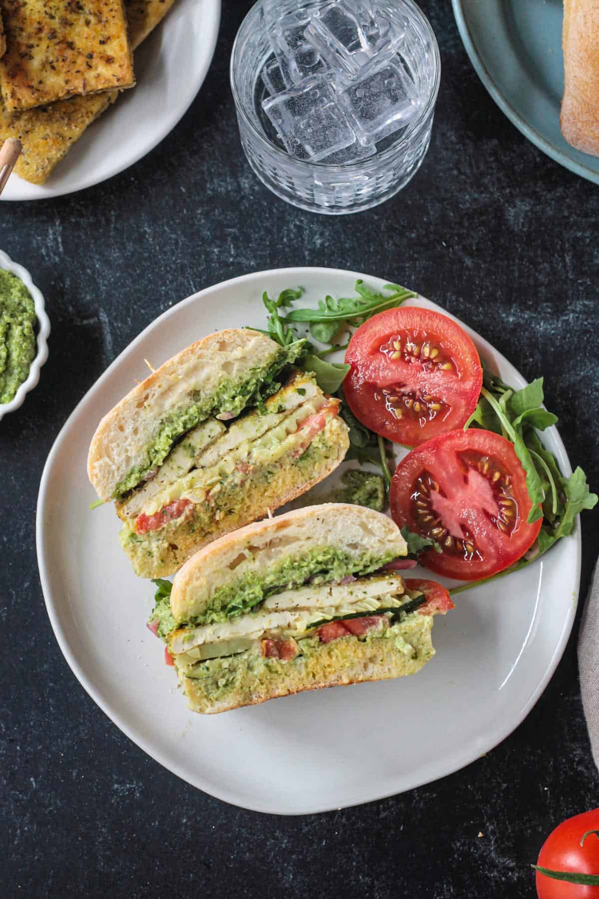 Two halves of a sandwich with tofu, tomato, arugula, and pesto.