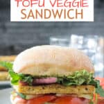 Pesto tofu sandwich on a roll with tomato slices and arugula.