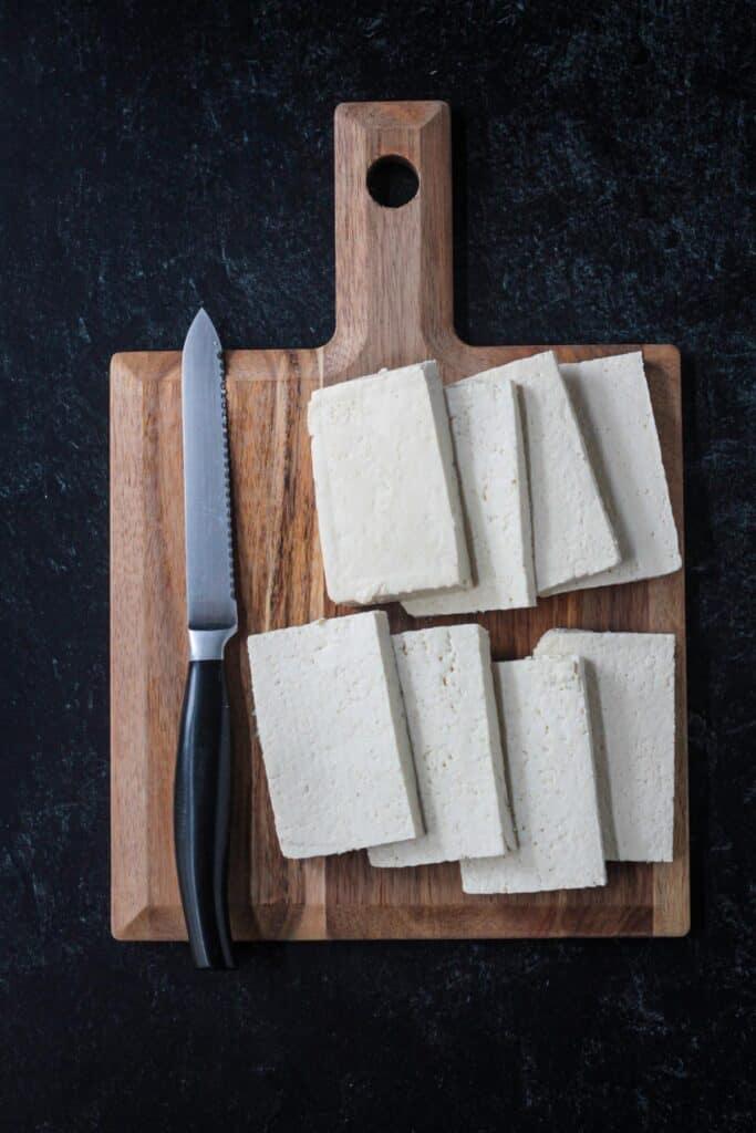 A block of tofu cut into eight slices on a cutting board.