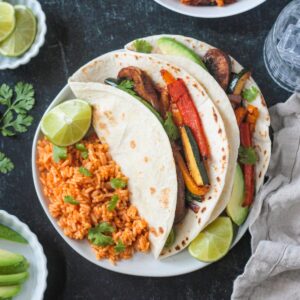 Two vegan fajitas on a plate with Spanish-style rice.