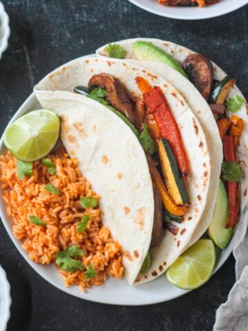 Two vegan fajitas on a plate with Spanish-style rice.