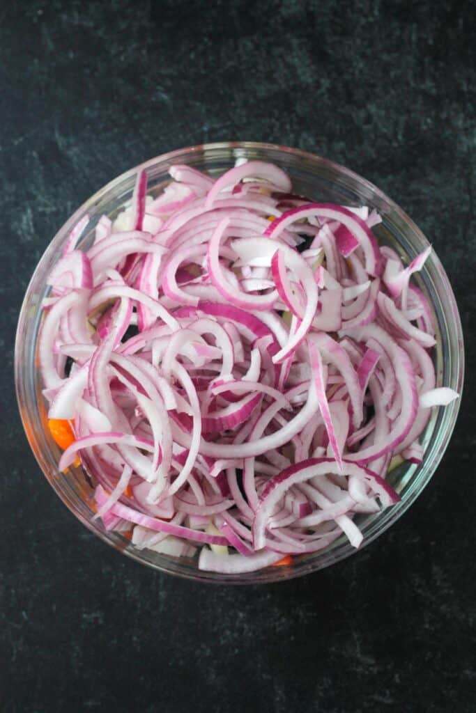 Sliced onions in a bowl with peppers and zucchini.