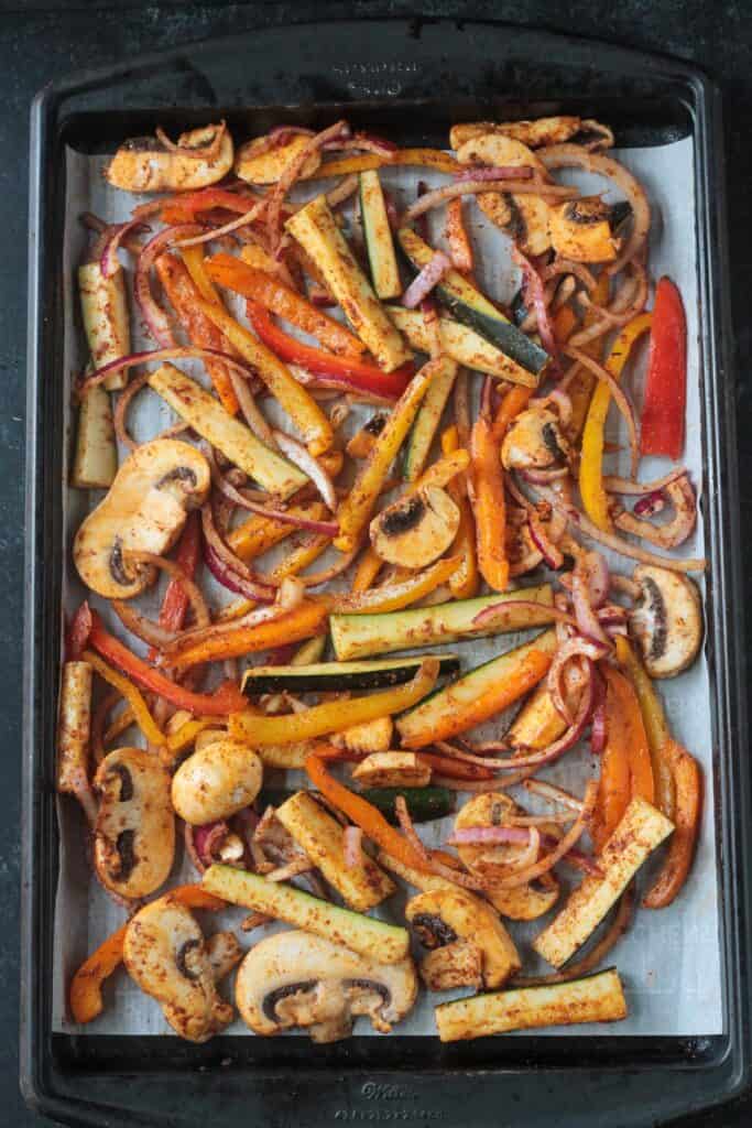 Spiced sliced veggies on a parchment lined baking sheet.