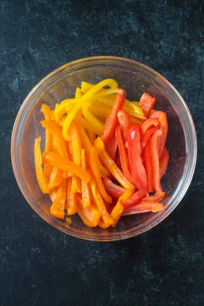 Sliced red, yellow, and orange bell peppers in a bowl.