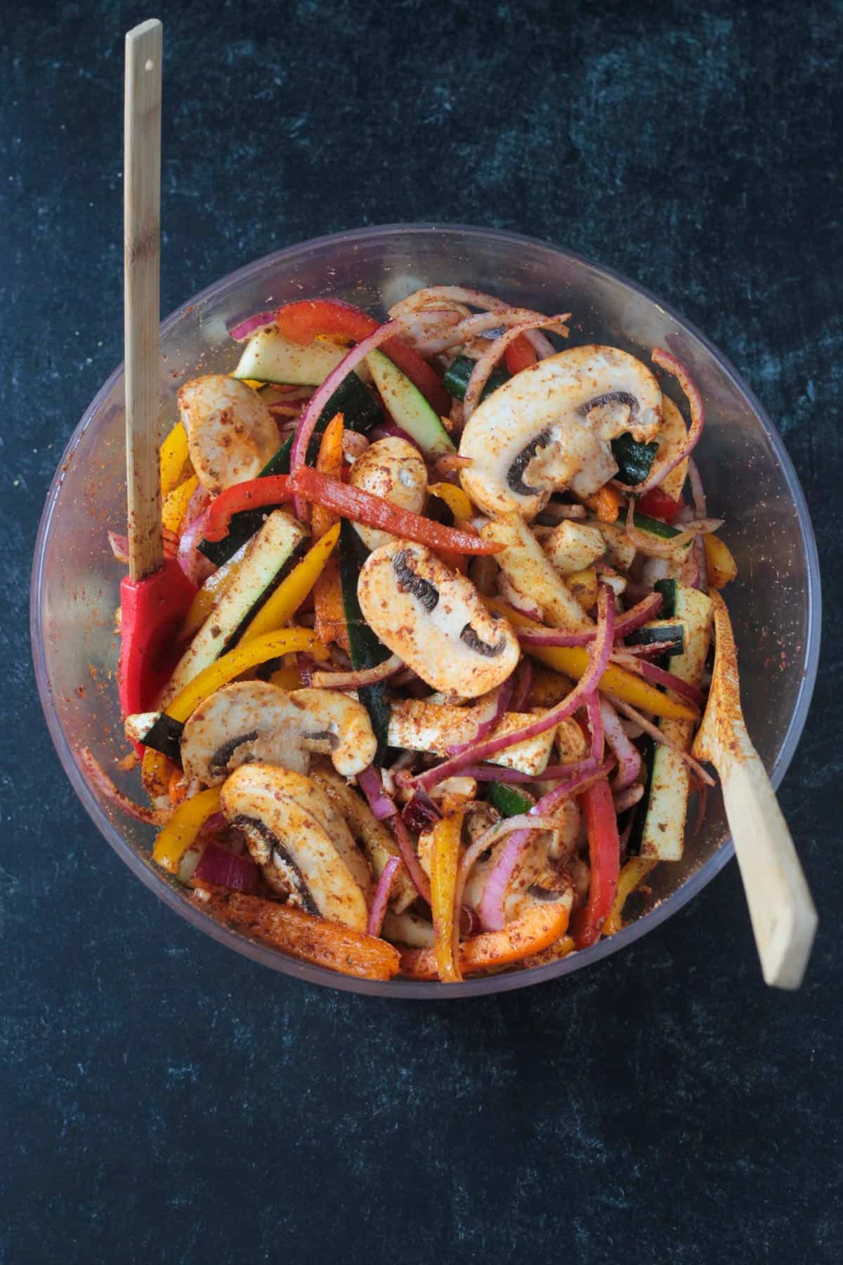 Sliced mushrooms, zucchini, peppers and onions in a bowl mixed with spices.