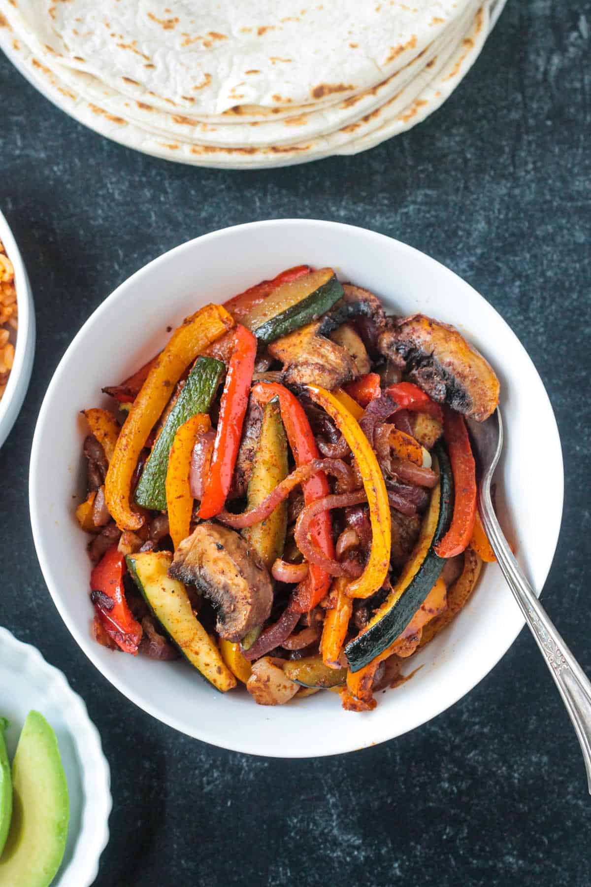 Roasted fajita veggies in a serving bowl with a spoon.