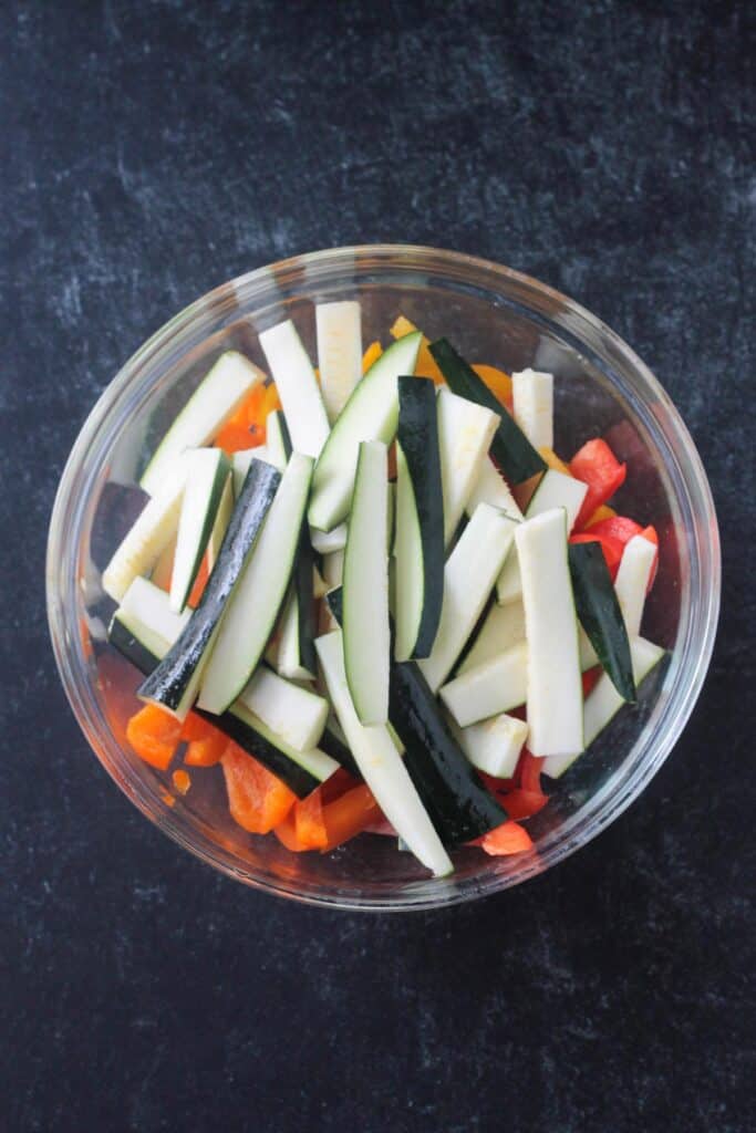 Sliced zucchini and bell peppers in a glass mixing bowl.