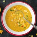 Creamy curried corn soup in a white bowl on a red plate.