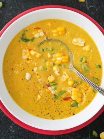 Creamy curried corn soup in a white bowl on a red plate.