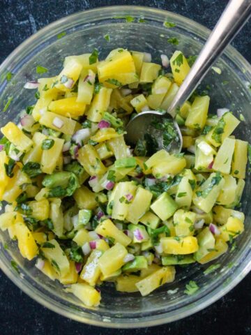 Diced pineapple, avocado, cilantro, and red onion mixed in a bowl.