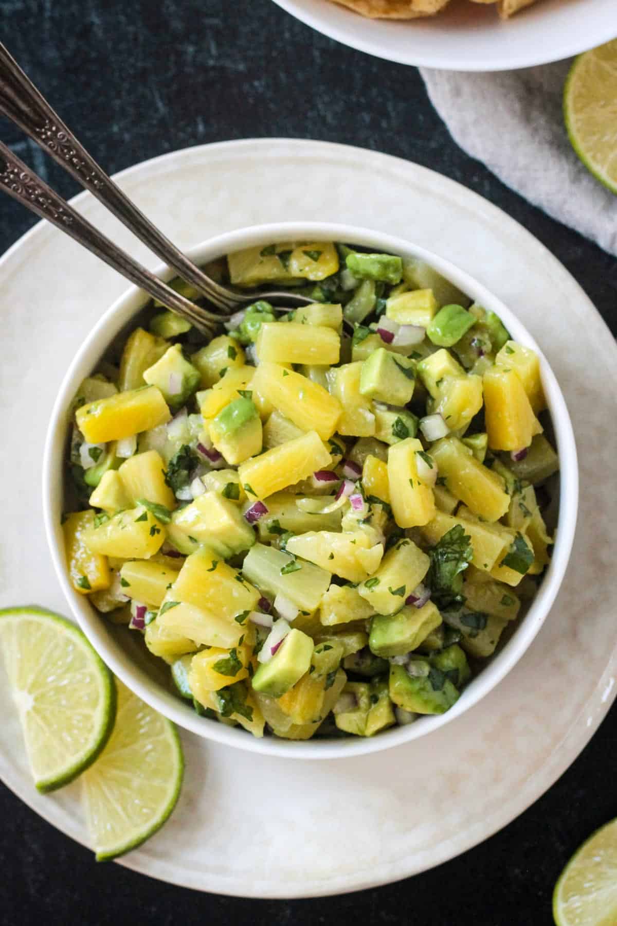 Pineapple avocado salsa in a serving bowl with two spoons.