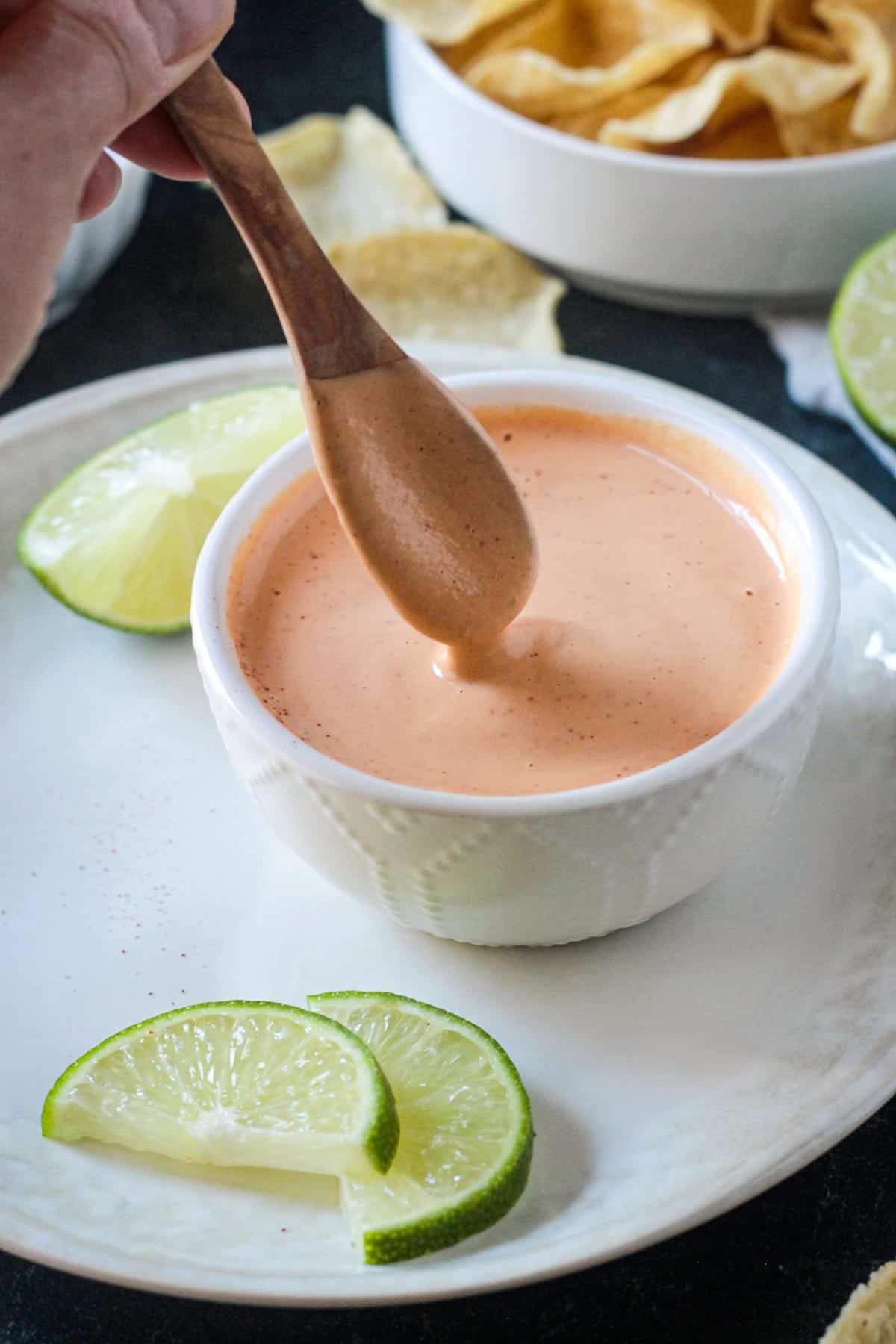 Small wooden spoon scooping up creamy chipotle crema from a small bowl.