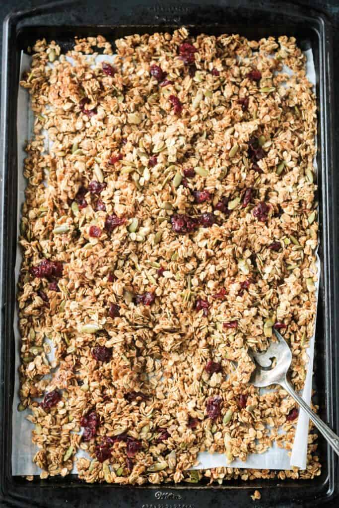 Dried cranberries mixed into the granola on a rimmed baking sheet.