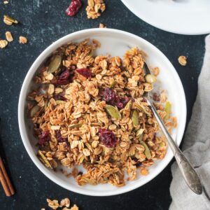 Bowl of pumpkin spice granola with pumpkin seeds and dried cranberries.