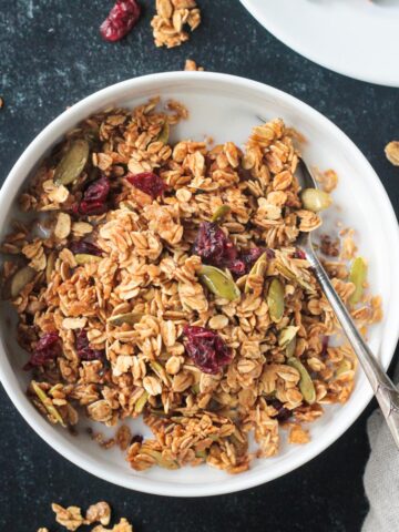 Bowl of pumpkin spice granola with pumpkin seeds and dried cranberries.