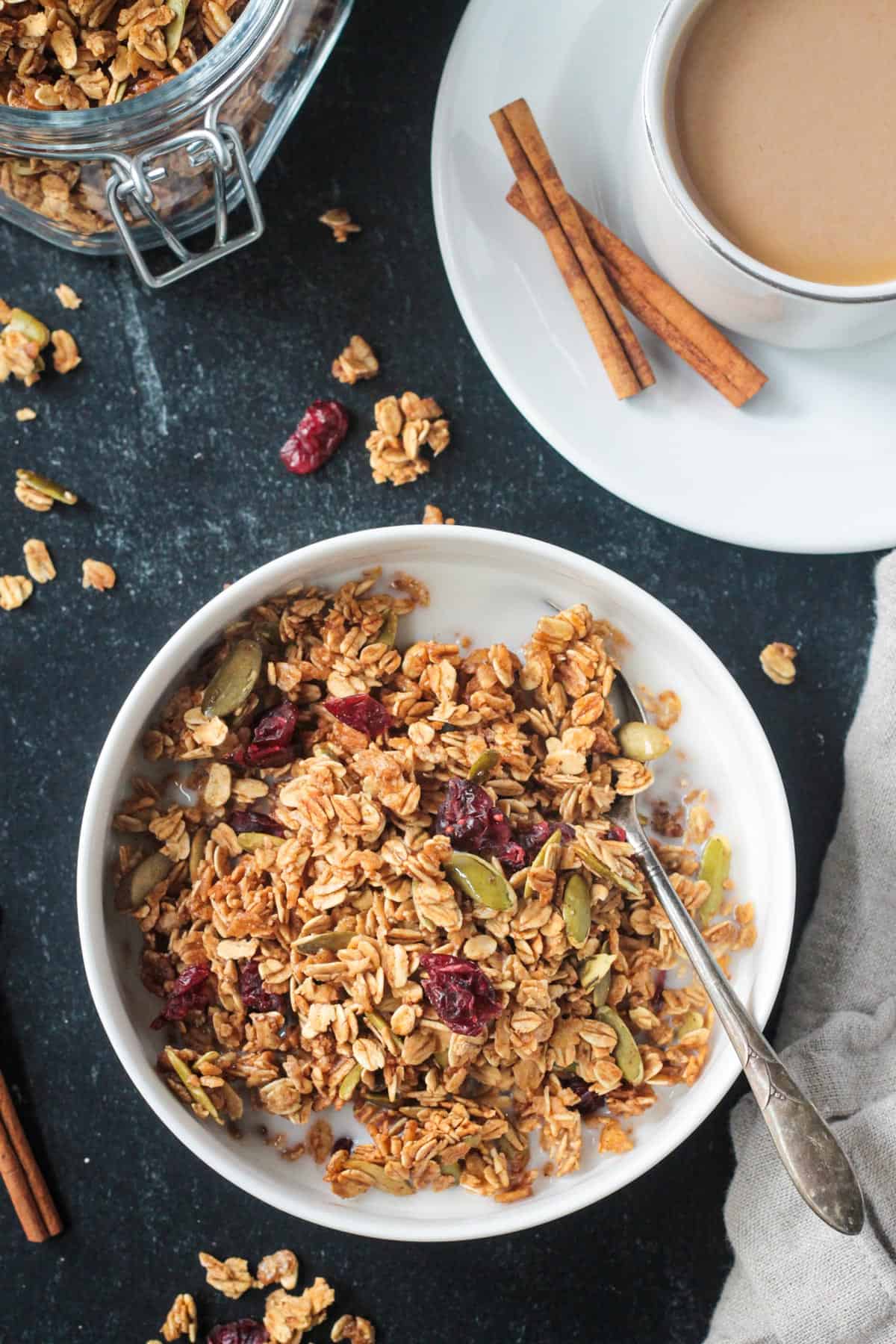Pumpkin spice granola with a splash of milk in a bowl next to a cup of coffee.