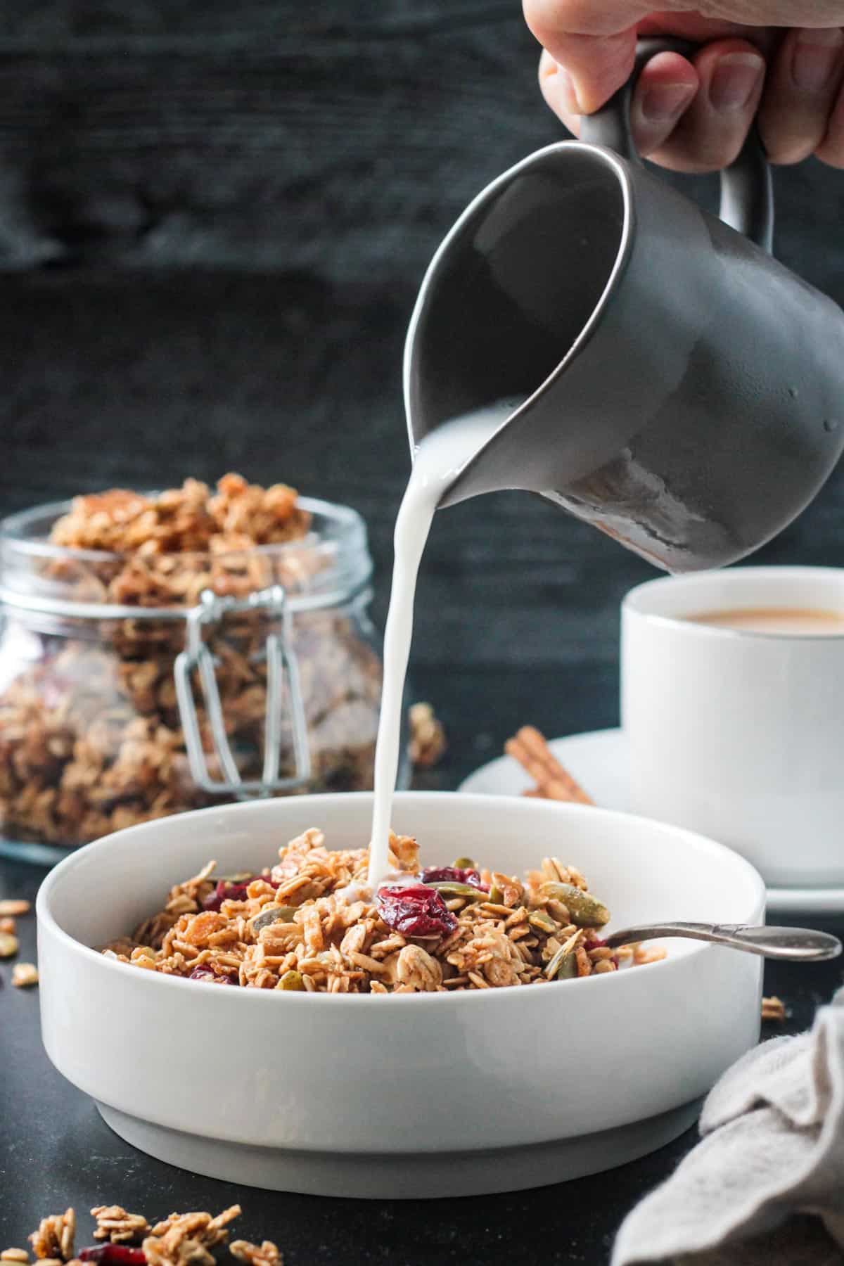 Milk being poured from a small pitcher into a bowl of granola.
