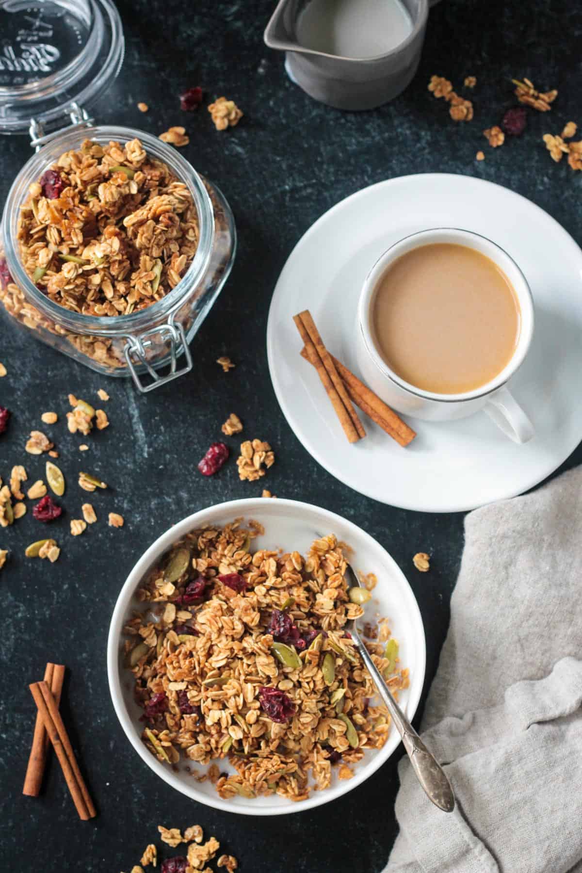 Bowl of granola next to a cup of coffee and a jar of more granola. 