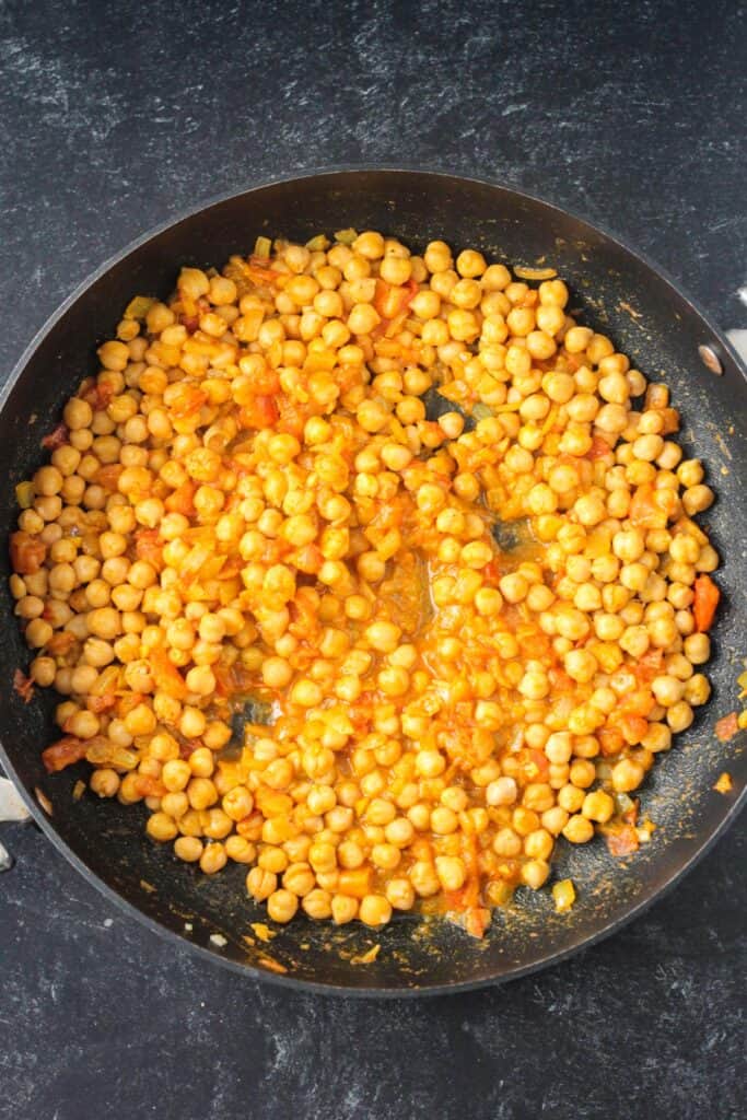 Chickpeas mixed with spices and onions in a large skillet.