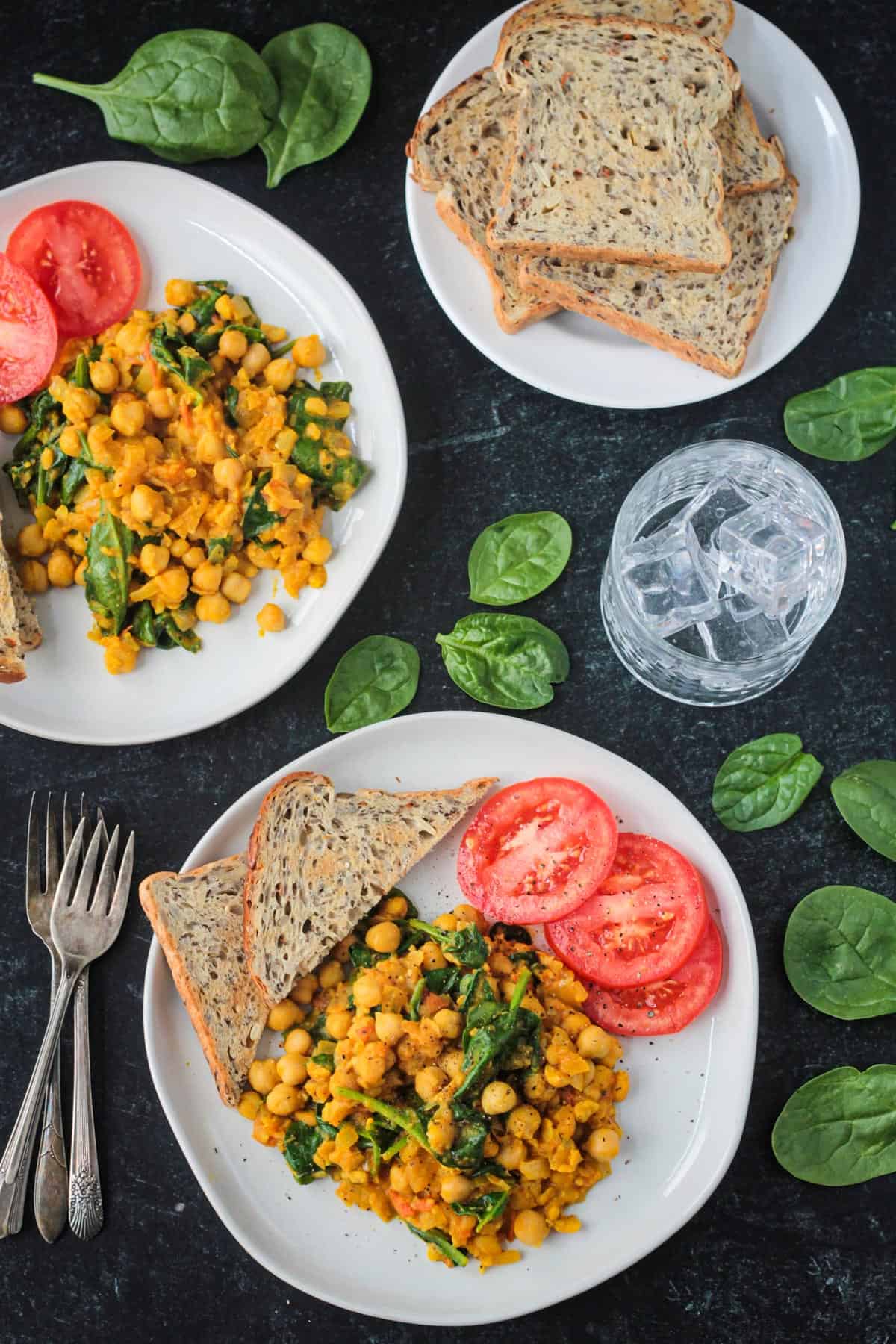 Two plates of chickpea spinach scramble with toast and tomato slices.