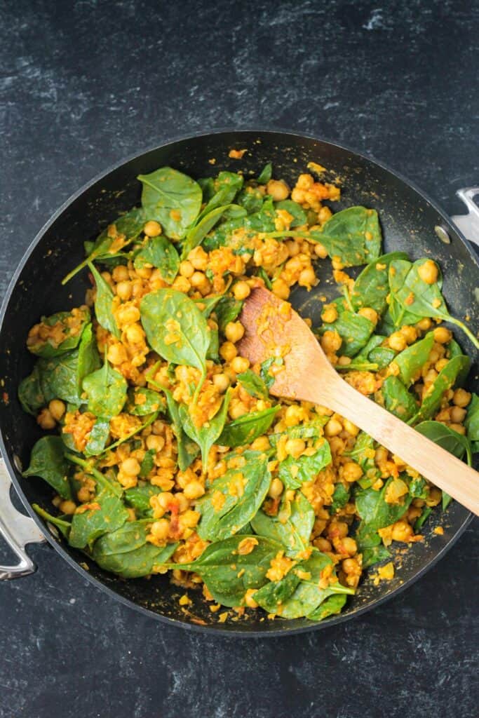 Fresh baby spinach added to the chickpea mixture in a skillet.
