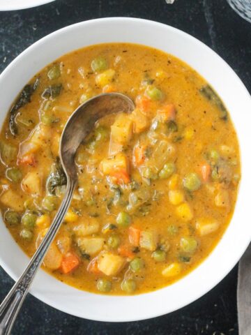 Metal spoon in a bowl of creamy vegetable soup.